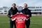 Das Bild zeigt Thomas Heim, President Climate Solutions Europe bei Carrier, und Rouven Kasper, Vorstand Marketing und Vertrieb FC Bayern auf dem Fußballplatz mit einem FC Bayern Trikot in der Hand.